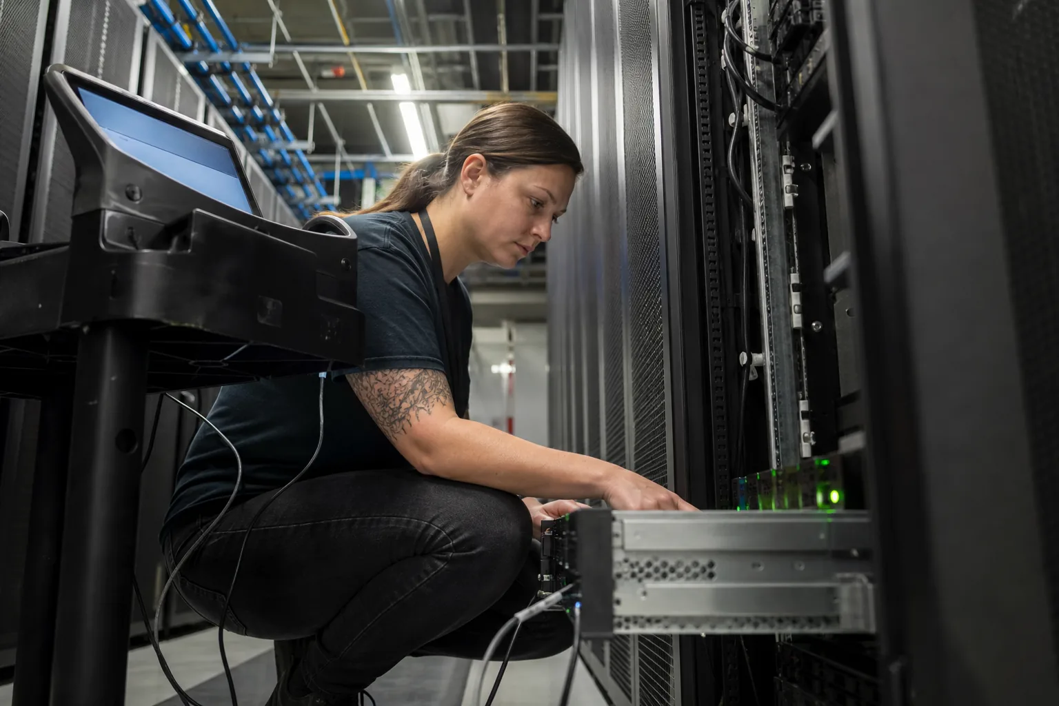 Engineer kneeling in a colocation aisle with a laptop on a crash cart connected to a dedicated server