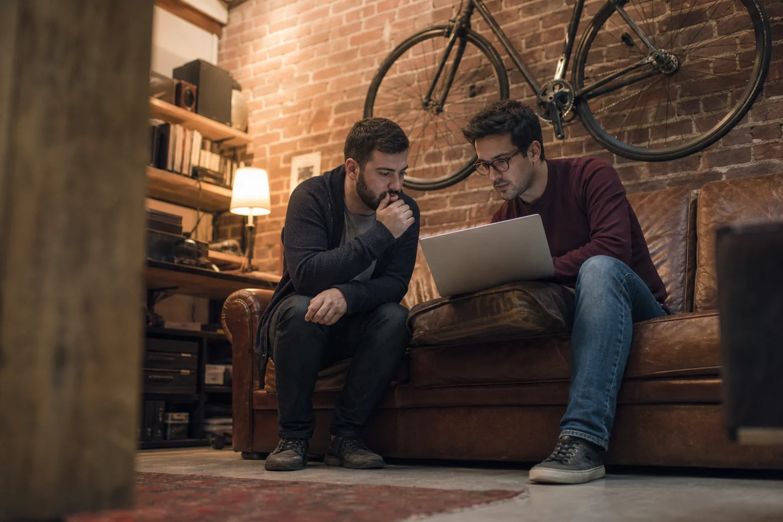 Two developers pairing on a sofa with one laptop in a small agency studio